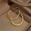Sleek gold crescent hoop earrings displayed in a beige jewelry box, highlighting their minimalist open design and polished finish.