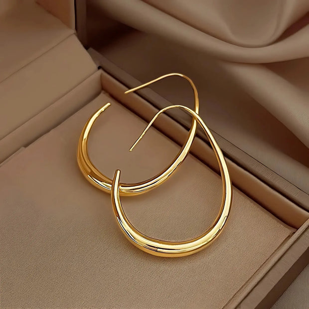 Sleek gold crescent hoop earrings displayed in a beige jewelry box, highlighting their minimalist open design and polished finish.