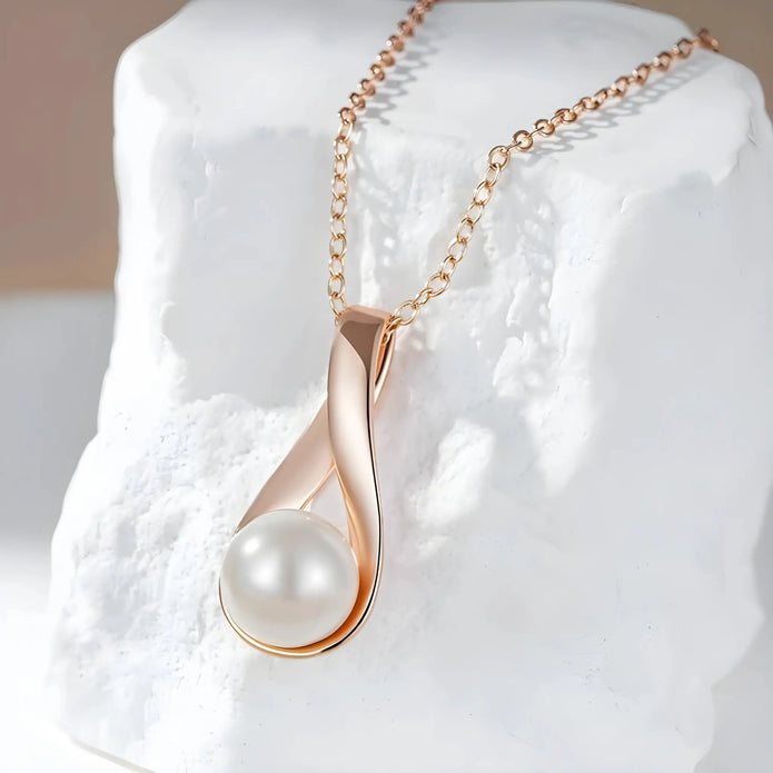 Rose gold necklace with a pearl pendant on a white rock.