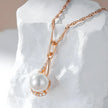Pearl necklace with rose gold chain on a textured white surface