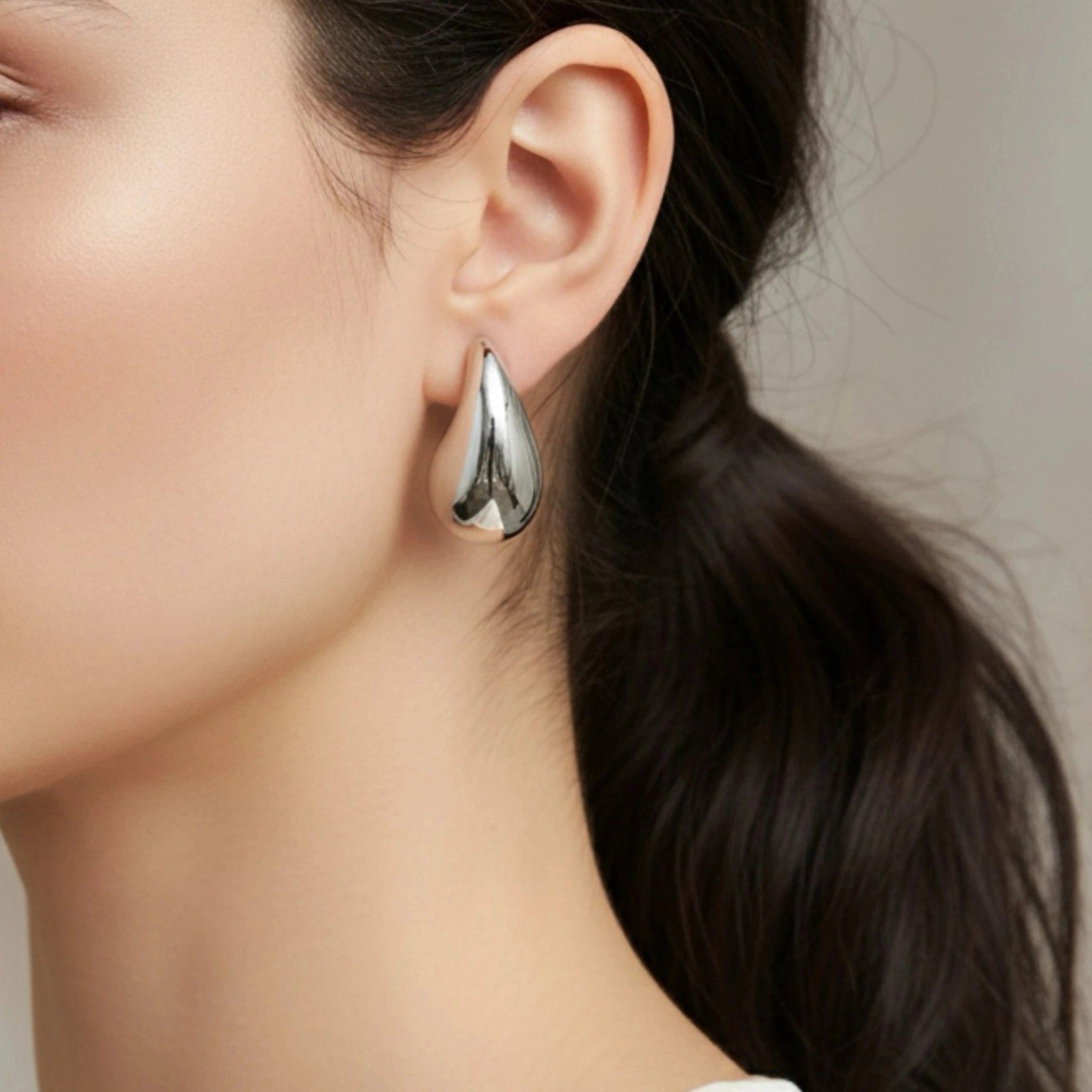Close-up of a woman wearing a silver teardrop earring against a neutral background